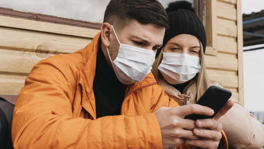 Seguro Viagem: quais seguradoras cobrem Covid? 3 Foto de um casal com mascara olhando pesquisando no celular