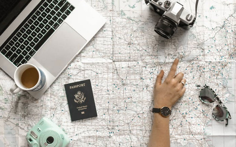Intercâmbio: quais países estão recebendo estudantes e dicas de viagem 5 Mão apontando no mapa com passaporte, câmera e notebook próximos.