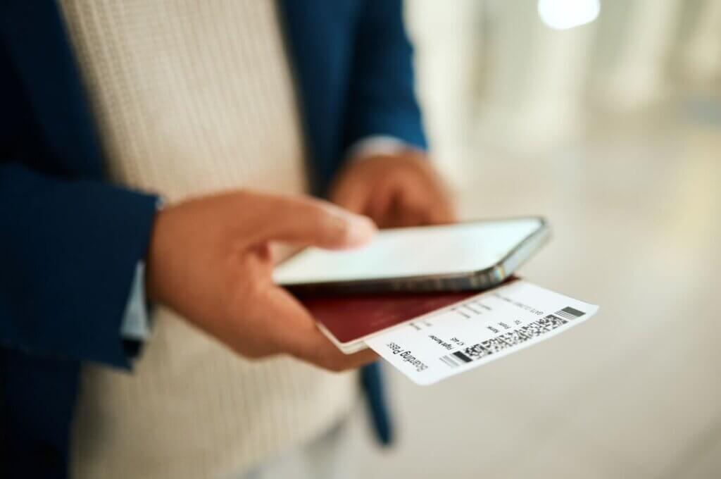 Mala extraviada: o que fazer para localizar a bagagem e acionar o seguro 4 Um homem segurando o seu celular com uma passagem e passaporte nas mãos.
