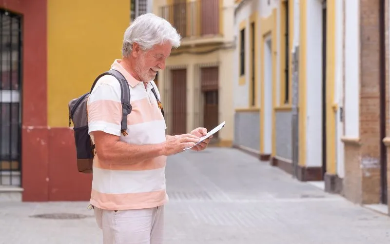 Homem feliz turista sênior com mochila andando nos becos da cidade velha de Sevilha, Espanha