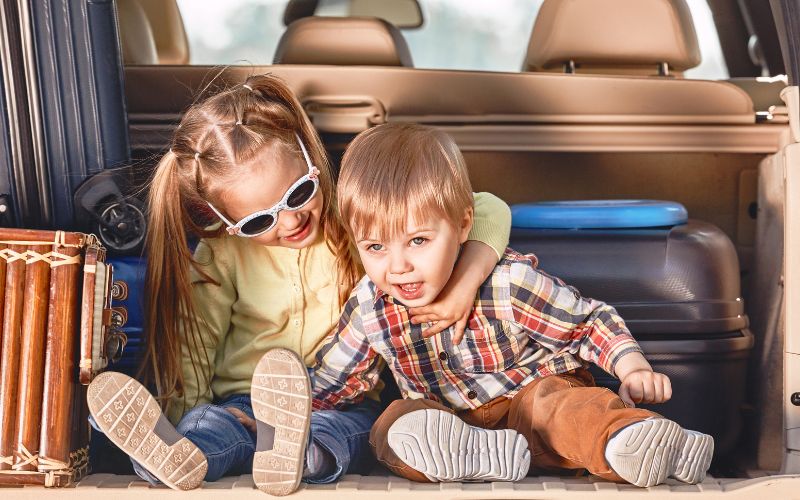 Viagem de Família com as Crianças para Destinos Divertidos 1 Início da viagem. Crianças fofas no porta-malas de um carro com malas. Viagem em família