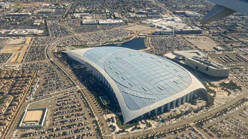 Imagem aérea do Sofi Stadium em Inglewood, Califórnia, destacando seu design moderno e sua localização próxima a áreas residenciais e comerciais.