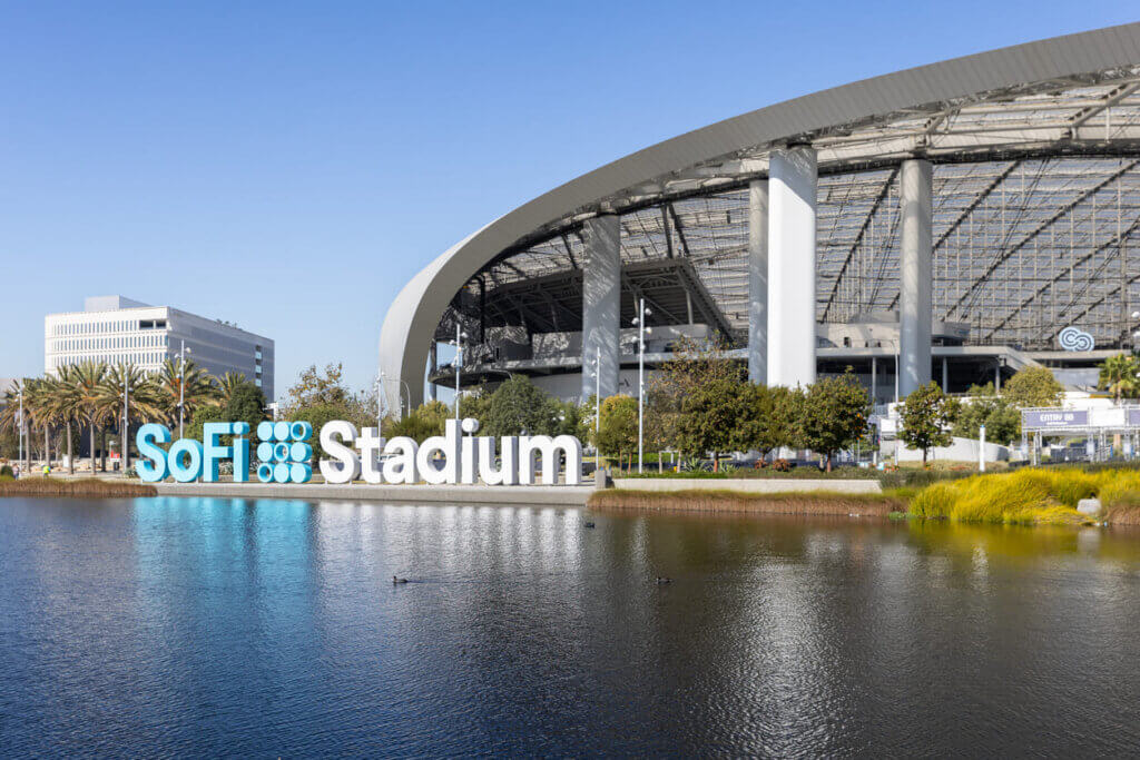 Imagem do SoFi Stadium em Los Angeles, destaque para sua estrutura moderna e integração com um corpo d'água ao redor, sob céu claro.