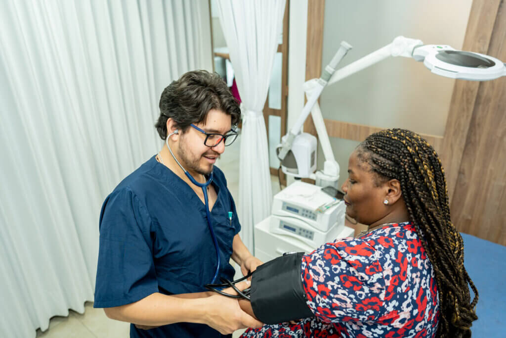 Viaje para Boston para a Copa do Mundo de Futebol 2026 5 Homem médico realizando exame de pressão arterial em paciente mulher em clínica médica, ambiente de atendimento com equipamentos de saúde ao fundo.