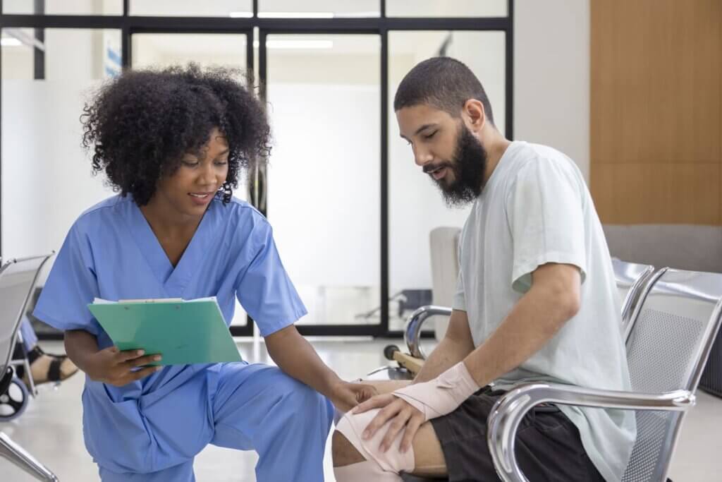 Profissional de saúde feminina prestando atendimento a homem com ferimento na perna em ambiente de hospital.