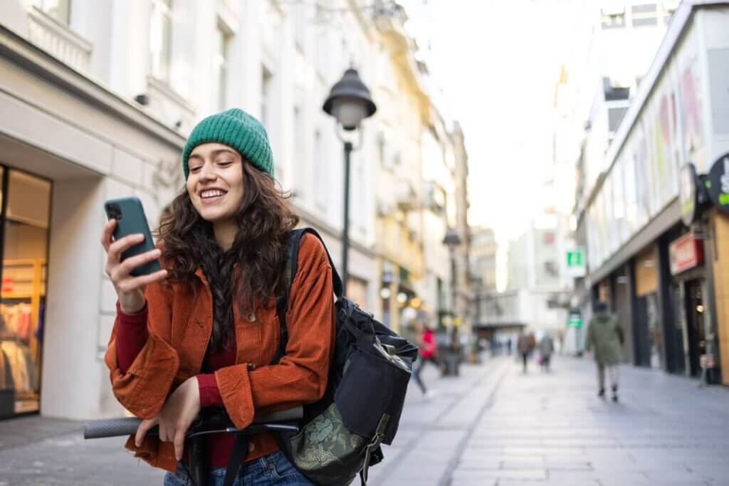 Custo de viagem internacional em 2026: como planejar cada despesa do seu roteiro 4 Mulher jovem usando um celular enquanto caminha na rua em clima de inverno.