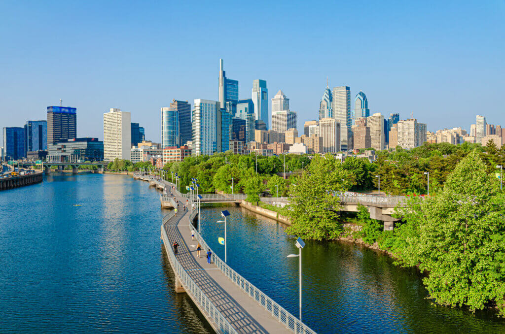Vista da cidade de Philadelphia com o rio Delaware ao fundo, oferecendo uma vista panorâmica do skyline com edifícios modernos e natureza ao redor em dia ensolarado. 