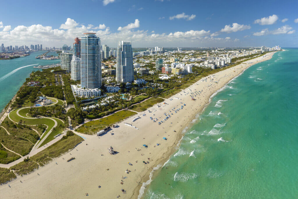 Praia de Miami com vista para o mar e arranha-céus ao fundo, destacando o cenário turístico e urbano de Miami Beach, Flórida.
