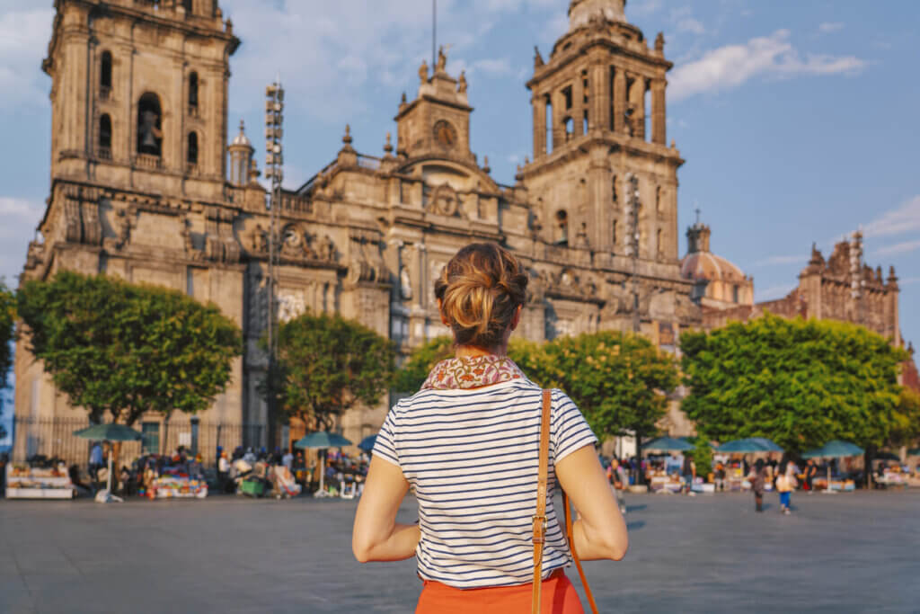 Uma mulher está na praça principal do Zócalo, olhando para a Catedral Metropolitana da Cidade do México enquanto o sol se põe.