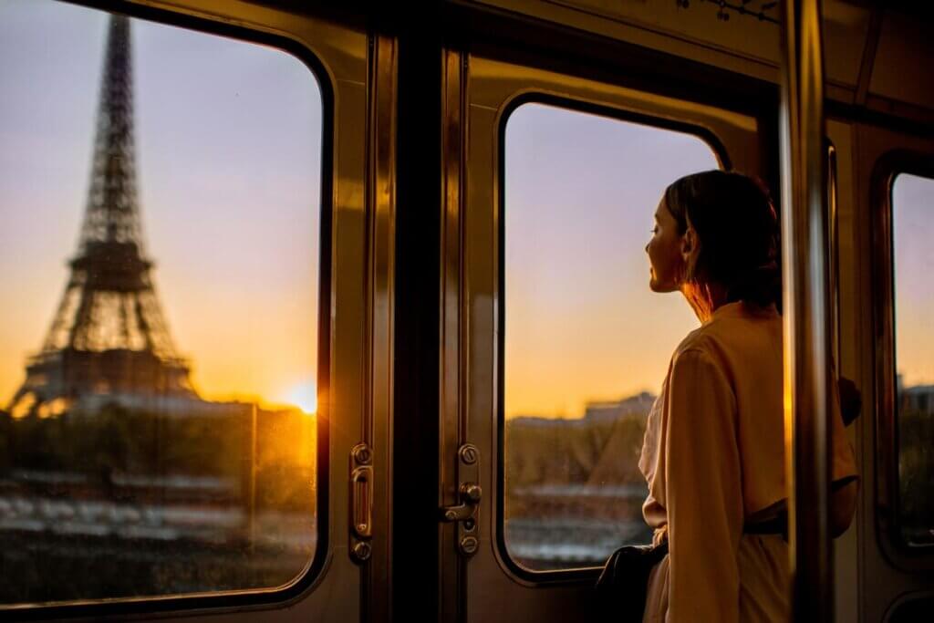Custo de viagem para Paris em 2026: quanto levar e como planejar 3 Mulher apreciando a vista de manhã na Torre Eiffel dentro do metrô durante o pôr do sol