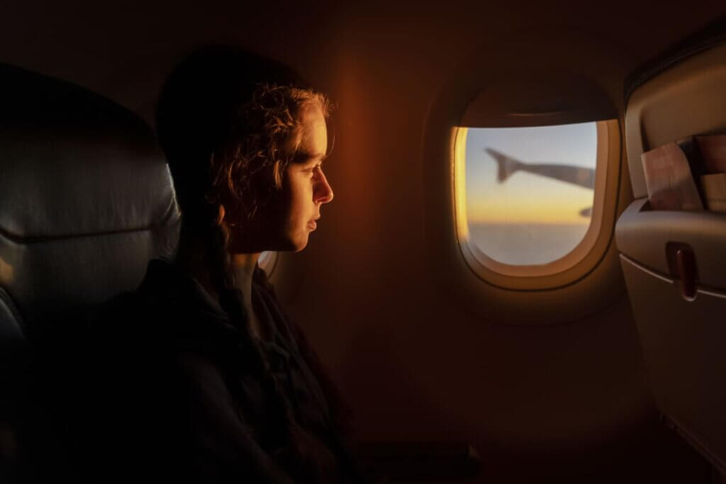 Viajar de avião pela primeira vez: guia completo para iniciantes em 2026 1 Jovem dentro de avião sentada e olhando o pôr do sol pela janela.