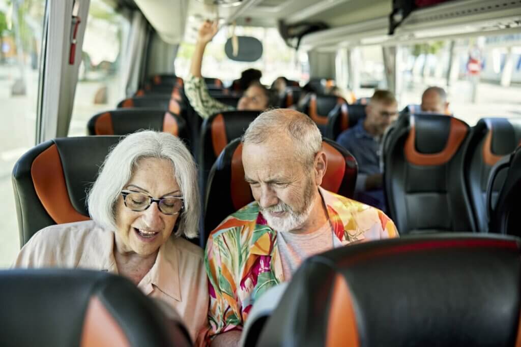 Seguro viagem para idosos: o que muda na cobertura e por que o plano padrão não basta 4 Um casal de idosos conversando dentro de um ônibus de viagem enquanto estão sentados.