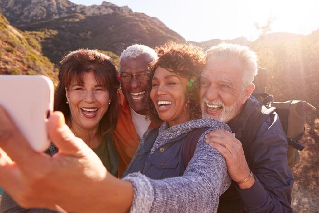 Seguro viagem para idosos: o que muda na cobertura e por que o plano padrão não basta 3 Grupo de amigos idosos composto por 4 pessoas enquanto estão sorrindo para tirar uma selfie e o pôr do sol ao fundo.