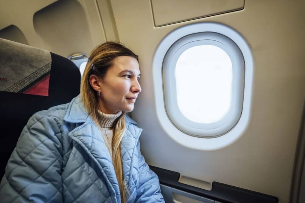 Como funciona o seguro viagem: da contratação ao acionamento, tudo o que você precisa saber 1 Mulher sentada em um avião e olhando pela janela
