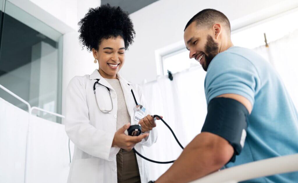 Como funciona o seguro viagem: da contratação ao acionamento, tudo o que você precisa saber 3 Uma médica aferindo a pressão de um paciente homem. Os dois estão sorridentes e tranquilos.