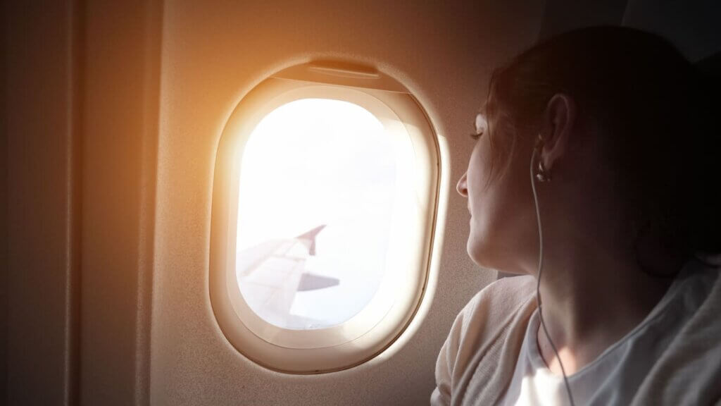 Diferença entre seguro saúde e seguro viagem: o que é cada um e qual contratar para viajar 4 O retrato da mulher nova está olhando a janela de um avião com luz do sol.